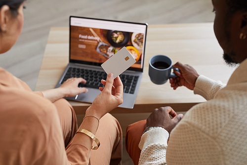 Rear view of couple sitting in front of the laptop and using credit card for online shopping