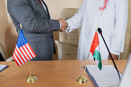 Two intercultural politicians shaking hands after signing agreement and striking international deal in formal environment