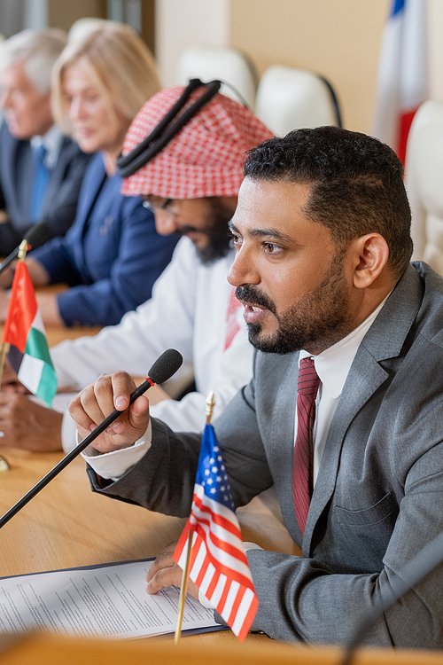 Confident mature businessman in formalwear speaking in microphone against row of foreign colleagues at conference