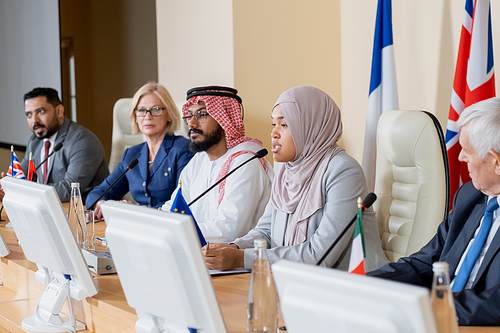 Young Muslim female delegate in hijab making report to foreign colleagues at summit or political forum