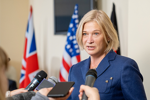 Mature female deputy in elegant suit speaking in microphones of journalists at press conference after political event