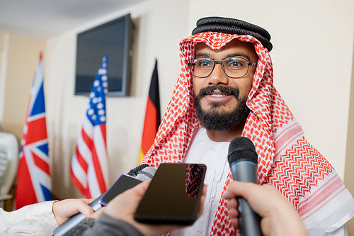 Young confident delegate in national clothes speaking in microphone held by journalist during press conference