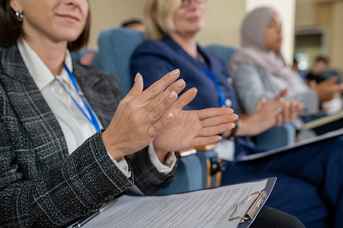 Young female delegate and her foreign colleagues clapping hands to speaker after presentation or report at conference