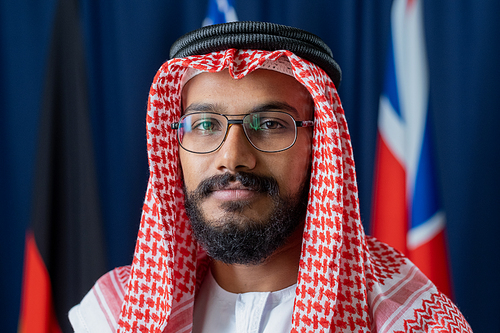 Contemporary young delegate or political leader in turban standing in front of camera while standing against flags