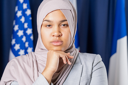 Young serious female delegate or political leader in hijab looking at camera while keeping hand under chin