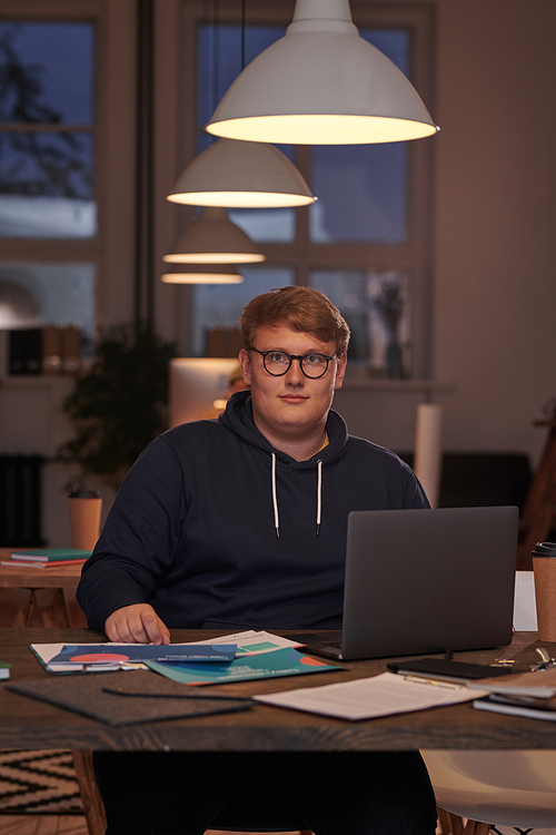 Portrait of young businessman in eyeglasses looking at camera while working at the table with laptop at office