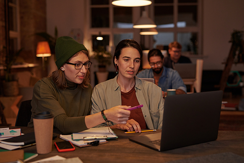 Two designers sitting at the table and using laptop at work they working in team at office