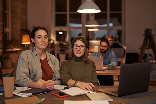 Portrait of young female designers looking at camera while working at the table with documents and laptop