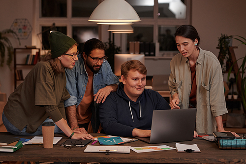 Group of designers using laptop together at the table making online presentation in team at office