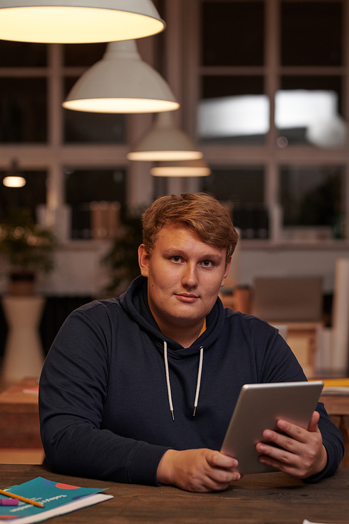 Portrait of young businessman in casual clothing looking at camera while working on digital tablet