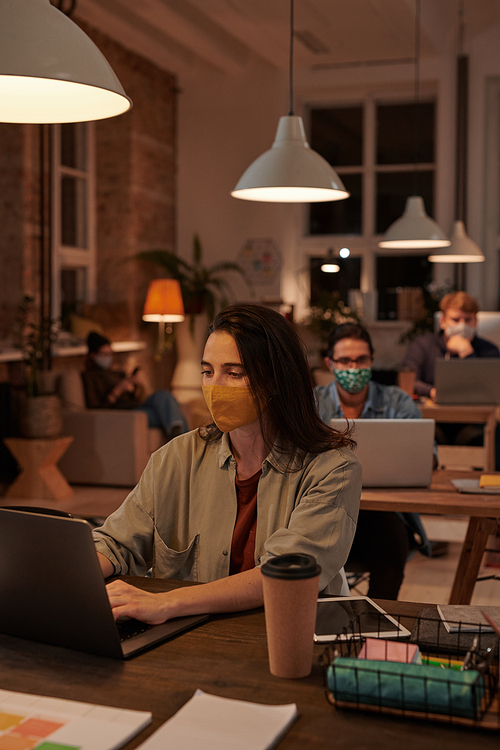 Group of business people in protective masks sitting at their workplaces and working on computers at office during pandemic