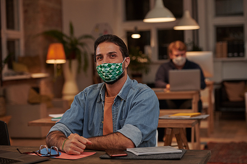 Portrait of young office worker in protective mask working at his workplace at modern office