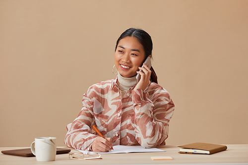 Portrait of Asian woman smiling at camera while sitting at the table and talking on mobile phone