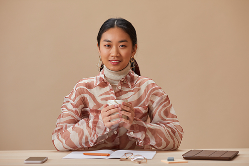 Portrait of Asian woman smiling at camera while drinking coffee during coffee break at the table