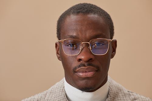 Close-up of African elegant man in eyeglasses looking at camera isolated on beige background