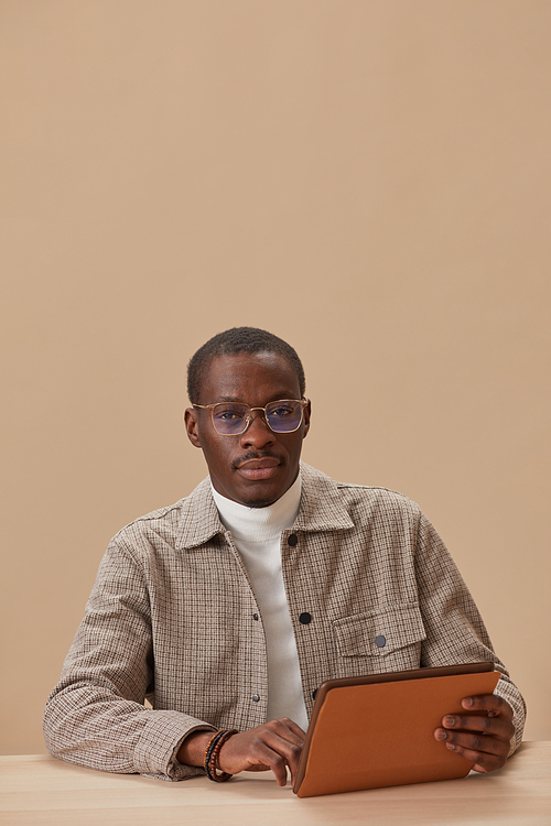 Portrait of African man in eyeglasses looking at camera sitting at the table with digital tablet