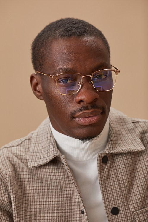 Portrait of African young man in eyeglasses and in elegant clothes looking at camera isolated on beige background