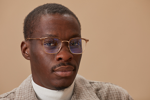 Close-up of African young man in eyeglasses looking at camera against the beige background