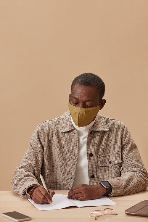 African man in protective mask writing at the table he studying during pandemic