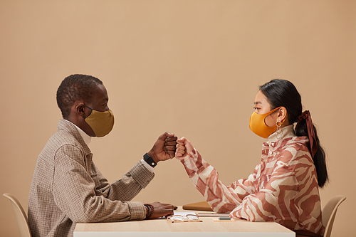 Two business partners in protective masks sitting at the table greeting each other before meeting