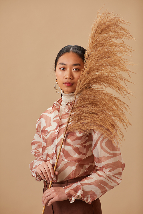 Portrait of Asian young woman holding plant looking at camera isolated on beige background