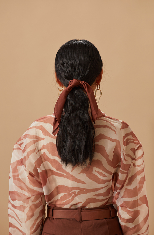 Rear view of young woman with dark long hair tied with ribbon against the beige background