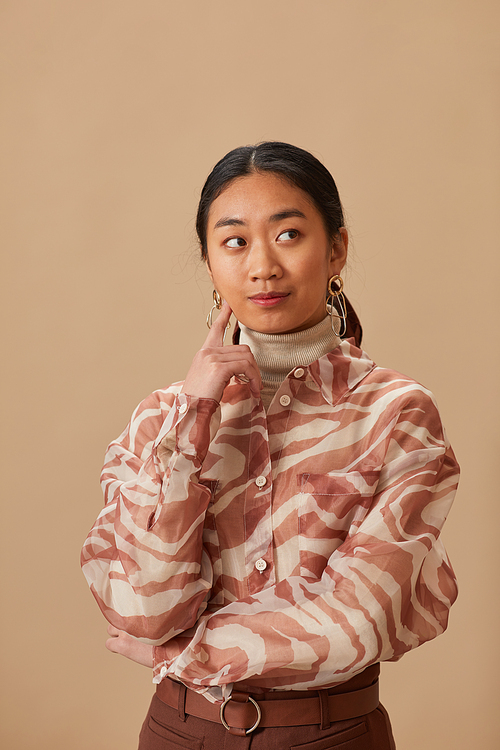 Portrait of Asian young woman with thoughtful sight standing against the beige background