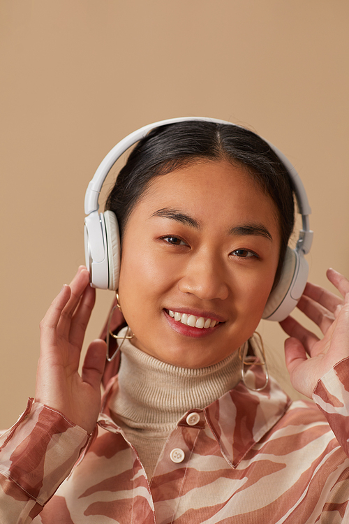 Portrait of Asian young woman in wireless headphone listening to music and smiling at camera