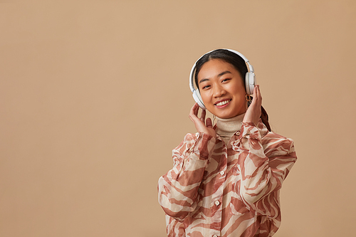 Portrait of Asian young woman in wireless headphones enjoying the music against the beige background