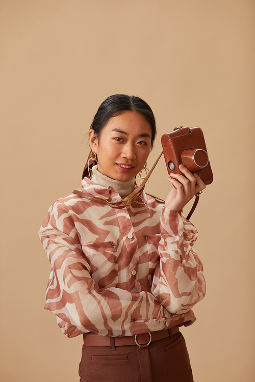 Portrait of Asian young woman holding old photo camera looking at camera isolated on beige background