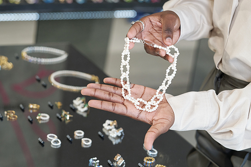 Hands of African shop assistant showing pearl necklace to customer over display with assortment of earrings and other jewelry