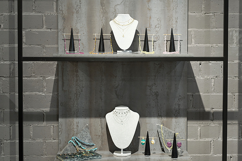 Two shelves with hangers for jewelry by grey wall inside large contemporary luxurious jewelry boutique