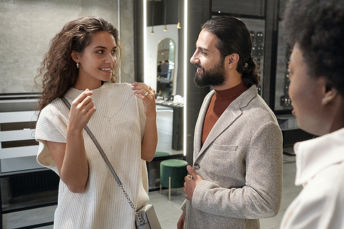 Happy young woman consulting with her husband while choosing new necklace in jewelry department inside trade center