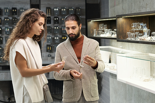 Young man and woman consulting about earrings while choosing jewelry in contemporary boutique or department