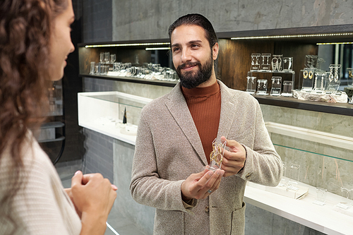 Happy young man and his girlfriend choosing new earrings while visiting large jewelry boutique in department store