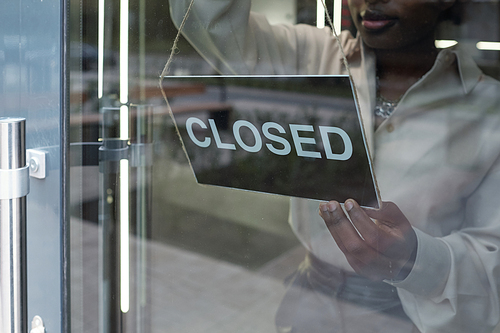 Hand of young African female owner of shop putting notice saying closed on glass door of boutique