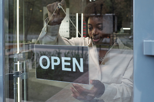 Young elegant shop assistant or small buisiness owner hanging sign announcing that boutique is open