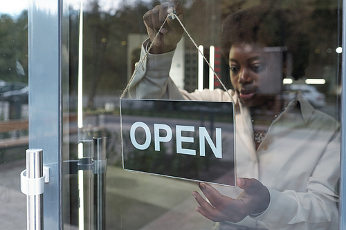 Young female owner of boutique hanging open notice on the door of large jewelry store in the morning