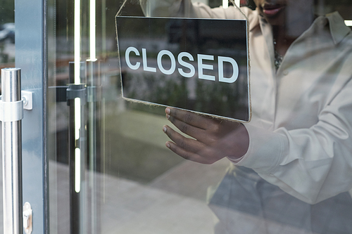 Shop assistant hanging closed sign on transparent door of boutique after finishing working day while standing inside