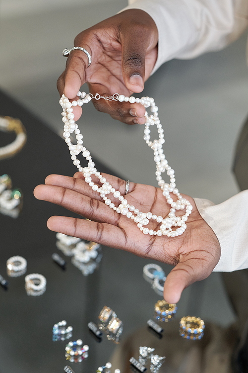 Hands of African woman holding handmade pearl necklace over display with other luxurious jewelry items
