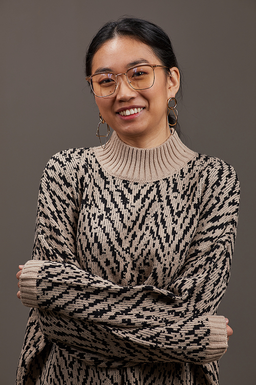 Portrait of Asian young woman in elegant clothing and in eyeglasses smiling at camera isolated on grey background