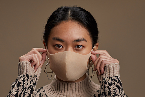 Close-up of Asian woman in protective mask looking at camera isolated on grey background