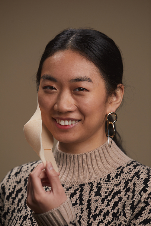 Portrait of Asian woman smiling at camera while wearing protective mask against the grey background