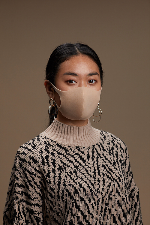 Portrait of Asian young woman in protective mask looking at camera against the grey background