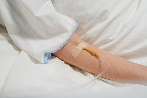 Close-up of patient lying on the bed under a drip in hospital ward
