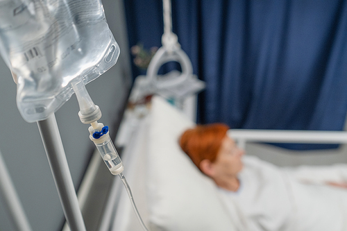 Close-up of iv drip hanging above the bed with patient in the hospital ward