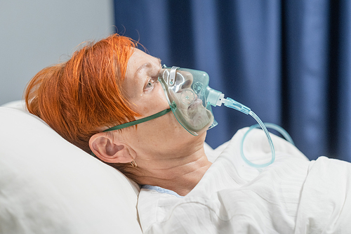 Close-up of senior woman patient receiving oxygen mask lying on a hospital bed during pandemic at hospital
