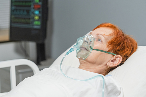 Elderly woman lying in hospital bed in oxygen mask on her face, she breathing hard during disease