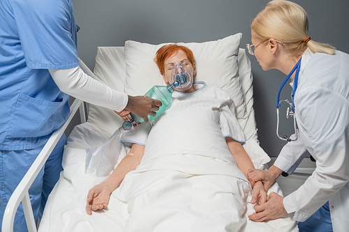 Female doctor examining the pulse of elderly woman while surgeon reanimating her with oxygen mask at hospital