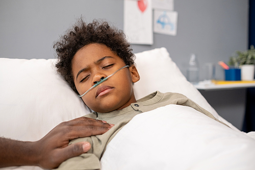 African little boy with tube in his nose lying unconscious in bed at hospital ward